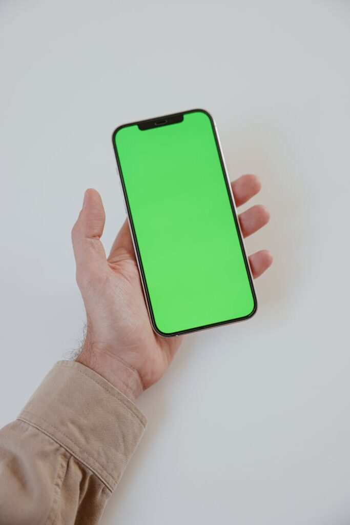 About Close-up of a hand holding a smartphone with a green screen, ideal for mockup and design presentations.